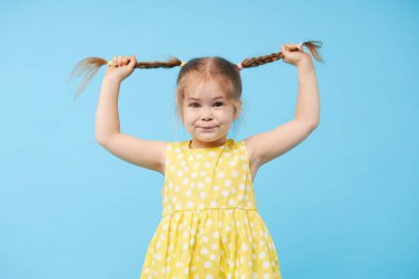 Şaşırmış, gülümseyen küçük bir kızın portresi. Çocuk mavi arka planda tek başına duruyor. Kameraya bakıp gülüyorlar.