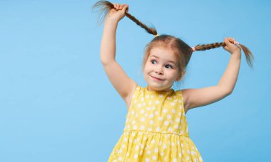Şaşırmış, gülümseyen küçük bir kızın portresi. Çocuk mavi arka planda tek başına duruyor. Kameraya bakıp gülüyorlar.