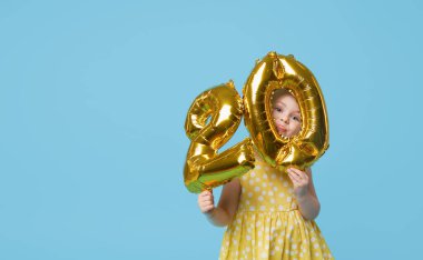 Küçük kız elinde folyo balonlarının yüzde 20 'sini tutuyor. İndirim, satış ve nakit para kavramı. Mavi stüdyo arka planı