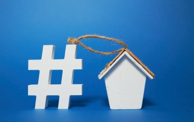 Evde kal konsepti. Hashtag sembolü ve mavi arka planda ahşap bir evin heykeli. Metin için boş alan.