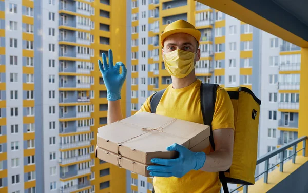 Safe food delivery. Courier in yellow uniform, protective mask and gloves delivers takeaway food during coronovirus quarantine