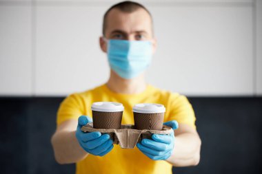 Koruyucu maskeli ve tıbbi eldivenli kurye paket yiyecek ve kahve getiriyor. Karantina, hastalık salgını, koronavirüs covid-19 salgını altında teslimat hizmeti.