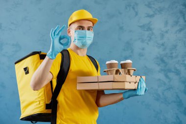 Koruyucu maskeli ve tıbbi eldivenli kurye paket yiyecek ve kahve getiriyor. Teslimat servisi karantina altında. Metin için alanı kopyala