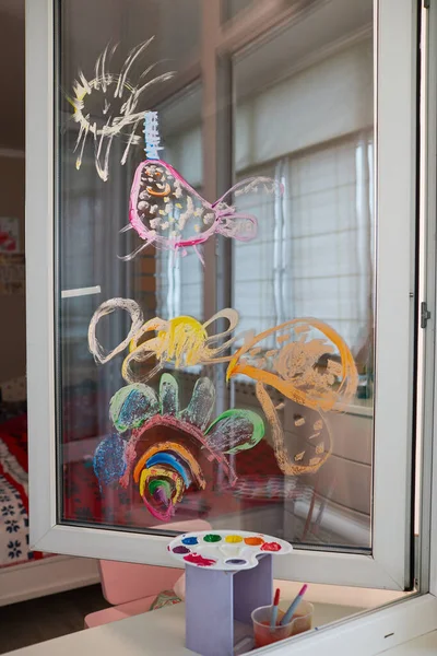 Childrens drawing on the glass window with paints. The concept of home self-isolation. Young artist learns to draw