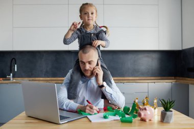 Babam karantina sırasında dizüstü bilgisayarla evde çalışıyordu. Küçük kız gürültü yapıyor ve babasının dikkatini mutfak ofisinden başka yöne çekiyor.