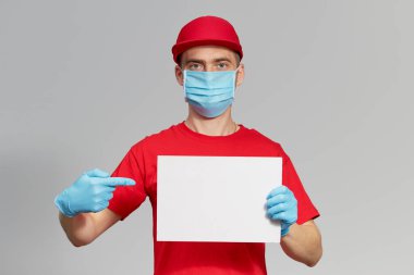 Kırmızı üniformalı, koruyucu maskeli ve eldivenli bir kurye mesaj için beyaz bir işaret tutuyor. Teslimat servisi karantina altında. 