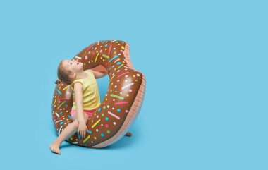 Başarısız yaz tatili. Donut şeklindeki lastik bir yüzüğün üzerinde dinlenen mutlu sürpriz çocuk modeli kız. Renkli mavi arka planda deniz tatili kavramı. 
