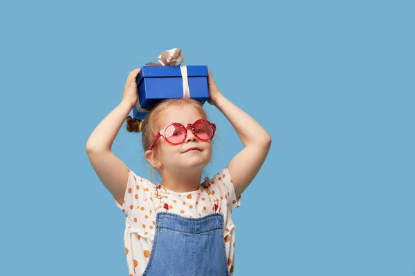 広告赤ちゃん製品 ギフトボックス付きの驚きの興奮した子供の女の子の肖像画 青い背景に隔離されています テキストの空のスペース — ストック写真