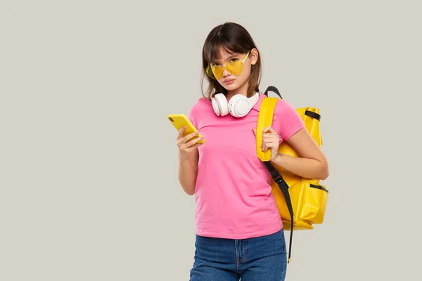 ハート型の眼鏡をかけたアジア系の少女が 灰色の背景に携帯電話を手にしている 新しいガジェットの広告 — ストック写真