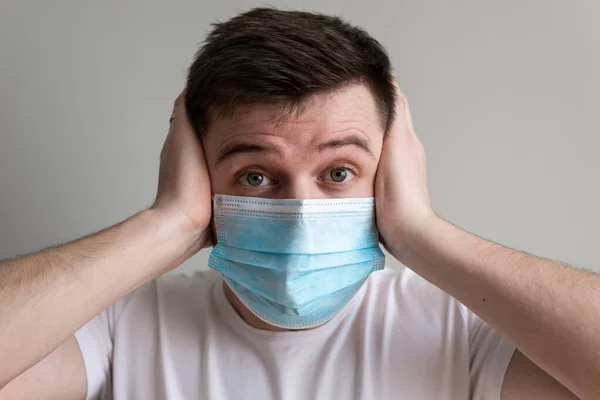 Sağlık maskesi takmış korkmuş kameraya bakıyor. Korkak bir adam koronavirüs korkusuyla virüslere ve virüslere karşı koruyucu tıbbi maske takıyor. Coronavirus 2019-ncov covid-19 konsepti.