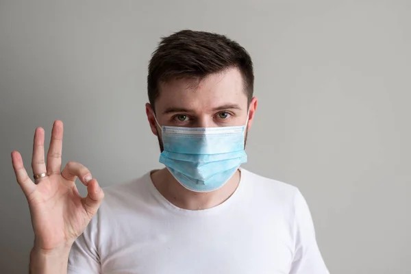 Yakışıklı adam iyi bir jest yapıyor. Sağlıklı adamın fotoğrafı bulaşıcı hastalıklara ve gribe karşı koruyucu maske takıyor. Sağlık hizmeti kavramı.