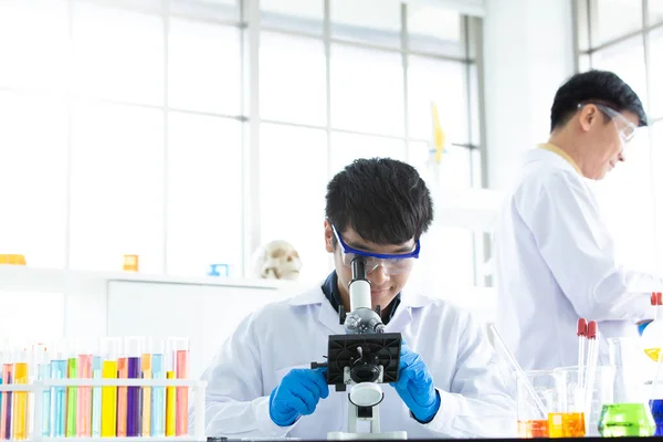 Male Research Scientists Talking, Using microscope while Working on Genetics Research Project and studying chemical or virus samples to detect pathologies, medical research in Innovative Laboratory.
