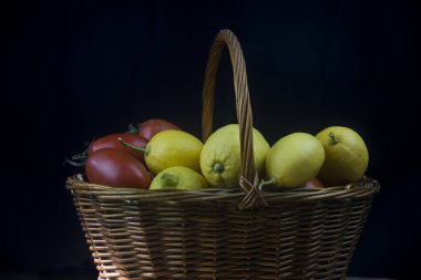 Siyah arka planda sonbahar meyveleri ve limonlarla dolu hasır sepet.