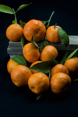 Siyah arkaplanda yaprakları olan organik mandalinalar