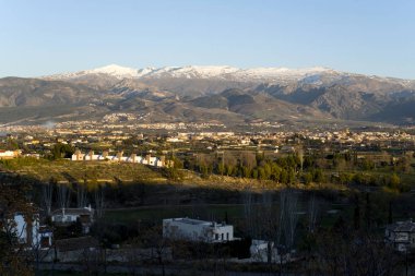 Karlı dağlarla kaplı manzara ve gün batımında evleri olan vadi.
