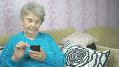 Yaşlı kadın bir cep telefonu kullanarak bir koltukta oturur