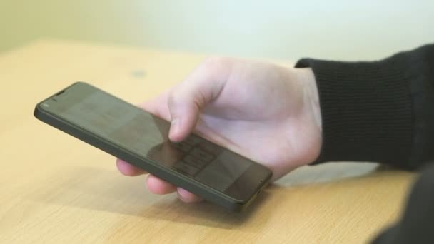 O menino sentado na mesa segura o telefone celular — Vídeo de Stock