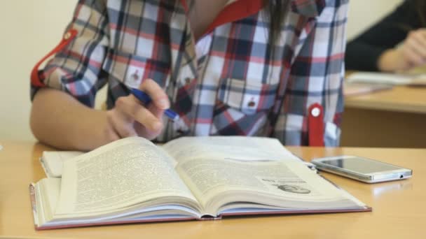 Chica sentada en el escritorio volteando páginas de libro de texto — Vídeos de Stock