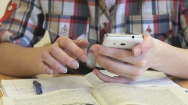 Colegiala sentada en un escritorio sostiene un teléfono inteligente — Vídeos de Stock