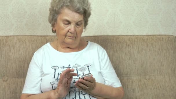 Old granny holding a mobile phone at home — Stock Video