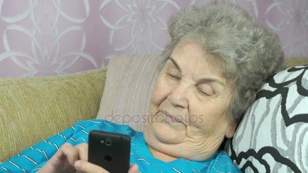 Bejaarde vrouw houdt een mobiele telefoon binnen — Stockvideo