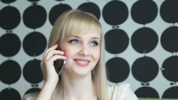 Chica sonriente hablando en un teléfono inteligente en un café — Vídeo de stock