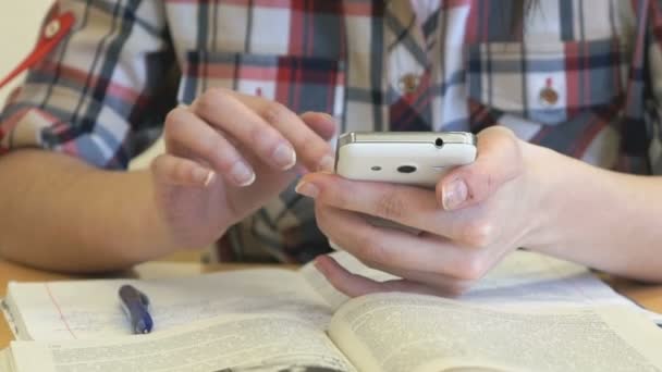 Estudante sentado em uma mesa detém um telefone celular — Vídeo de Stock