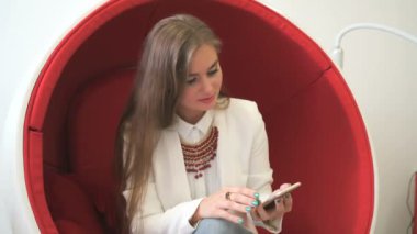Smartphone ile kırmızı sandalyede oturan kadın istemci