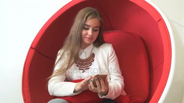 Smartphone ile kırmızı sandalyede oturan kız istemci