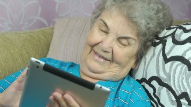 Yaşlı kadın bir tablet bilgisayar kullanarak rahatlatır