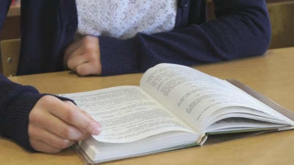 Девушка, сидящая за школьным столом, читает книгу — стоковое видео