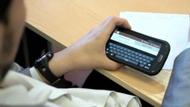 L'étudiant assis à un bureau tient un téléphone portable — Video