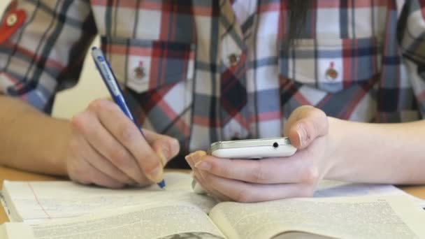 El adolescente sentado en un escritorio sostiene un teléfono inteligente — Vídeo de stock