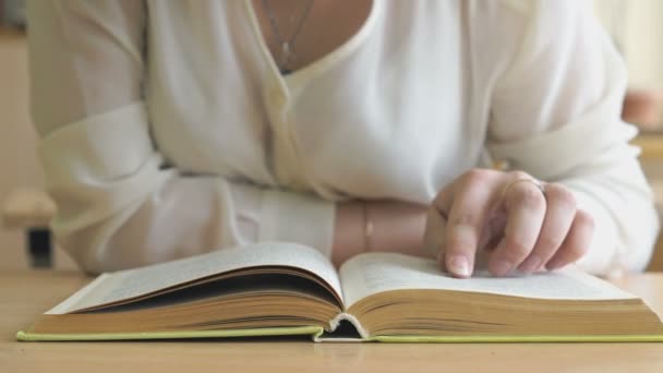 Colegiala sentada en el escritorio voltea páginas de libro — Vídeo de stock