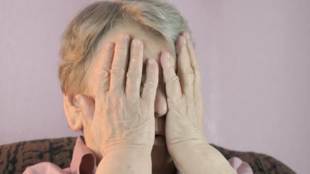 Alte Frau sitzt drinnen bedeckt Gesicht ihre Hände — Stockvideo