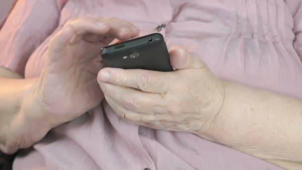 Uma mulher velha digita o texto em um smartphone preto — Vídeo de Stock