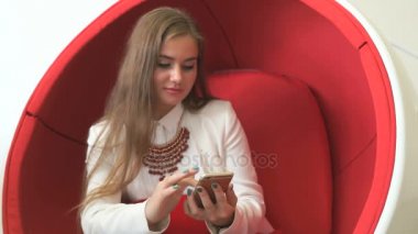 Smartphone ile kırmızı sandalyede oturan kız istemci