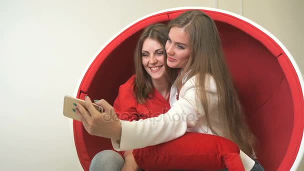 Dwie dziewczyny siedzi w czerwone krzesło, Dokonywanie selfie — Wideo stockowe