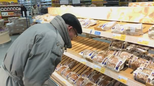 Пожилой человек выбирает хлеб в супермаркете Лента — стоковое видео
