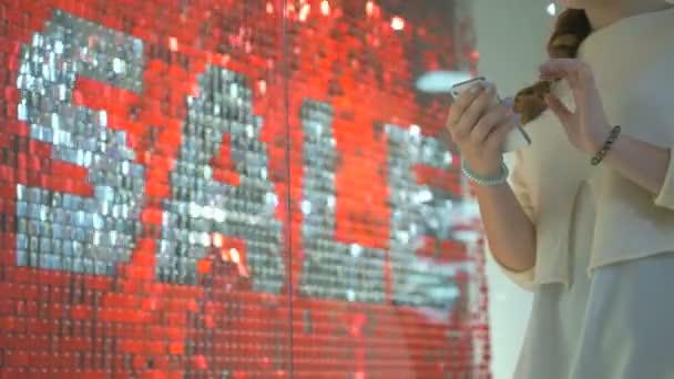 Дівчина стоїть на тлі червоного напису зі словом SALE — стокове відео
