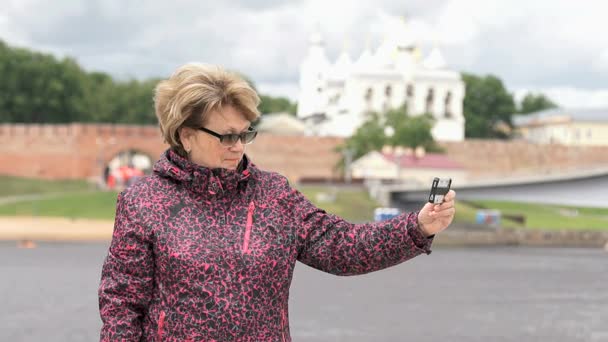 Взрослая женщина в возрасте 60 лет фотографирует со смартфона — стоковое видео