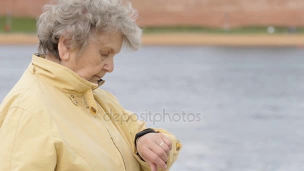 Mulher velha olha para o rastreador de fitness pulseira — Vídeo de Stock