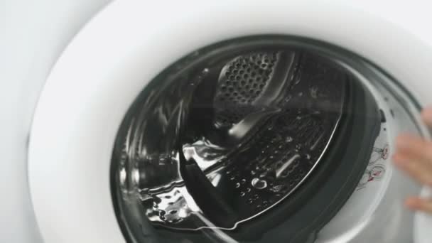 Рука кладет полотенце внутрь стальной стиральной машины барабан — стоковое видео