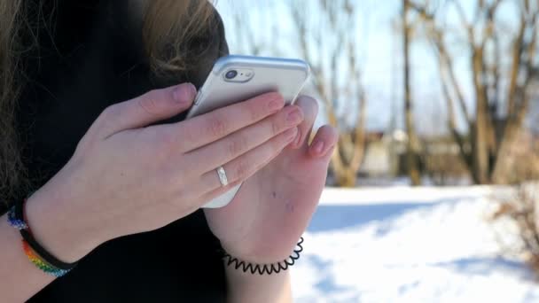 Adolescente sosteniendo un teléfono inteligente plateado al aire libre — Vídeos de Stock