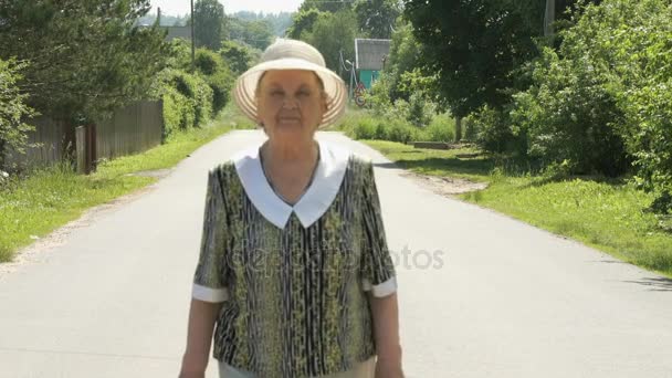 Стара жінка, що йде по дорозі в сонячний день — стокове відео