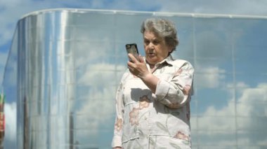 Yaşlı kadın bir akıllı telefon açık havada kullanarak konuşuyor