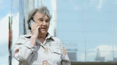 Yaşlı kadın bir akıllı telefon açık havada kullanarak konuşuyor