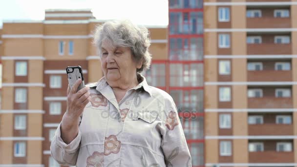 Bejaarde vrouw praat met behulp van een slimme telefoon buitenshuis — Stockvideo