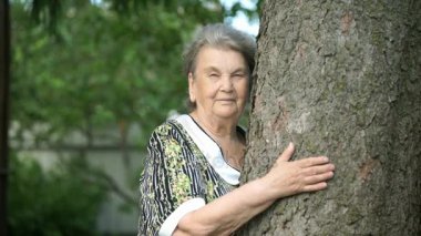 Yaşlı kadın kamera için ağaç gülümsüyor sarılma