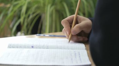 Kız öğrenci metin kalem kullanarak not defterinde yazıyor.